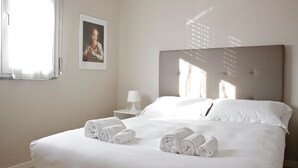 Una cama bien hecha con toallas enrolladas, una mesita de noche con una lámpara y un cuadro en la pared.