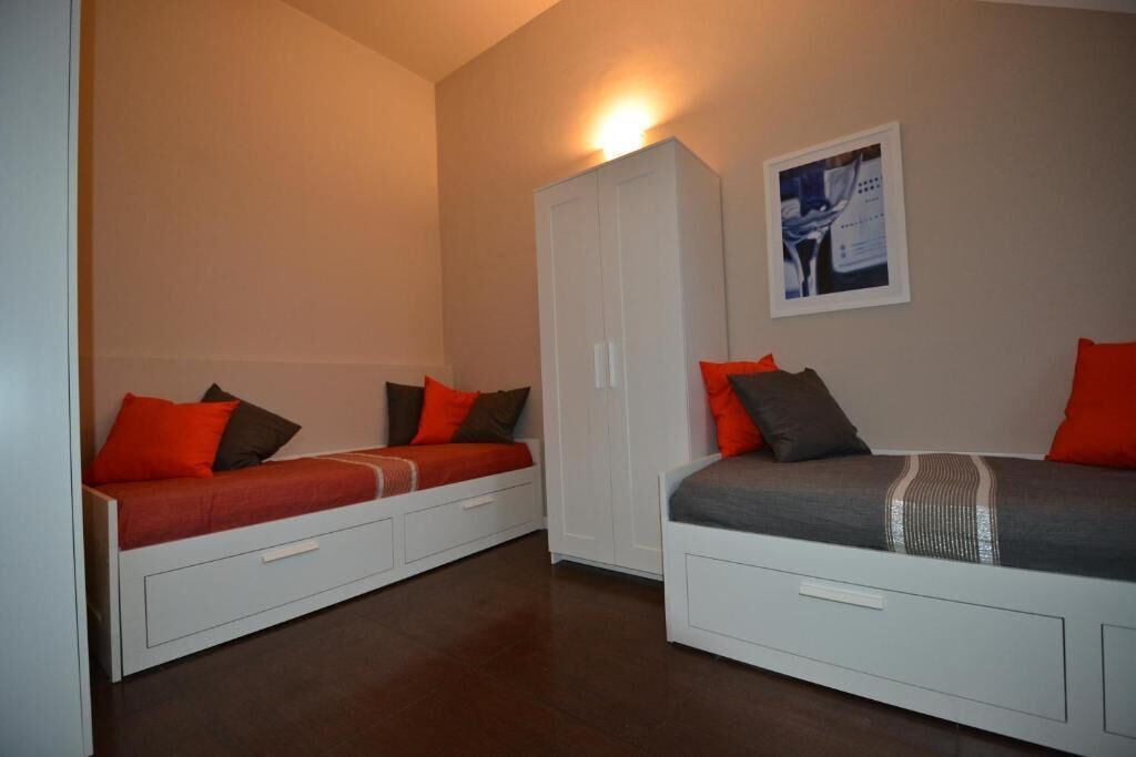 A bedroom with two beds, each with a storage drawer, a wardrobe, and a framed picture on the wall.