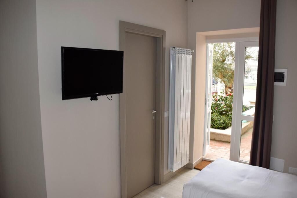 A hotel room with a bed, a television mounted on the wall, a sliding glass door leading to an outdoor area, and a radiator.