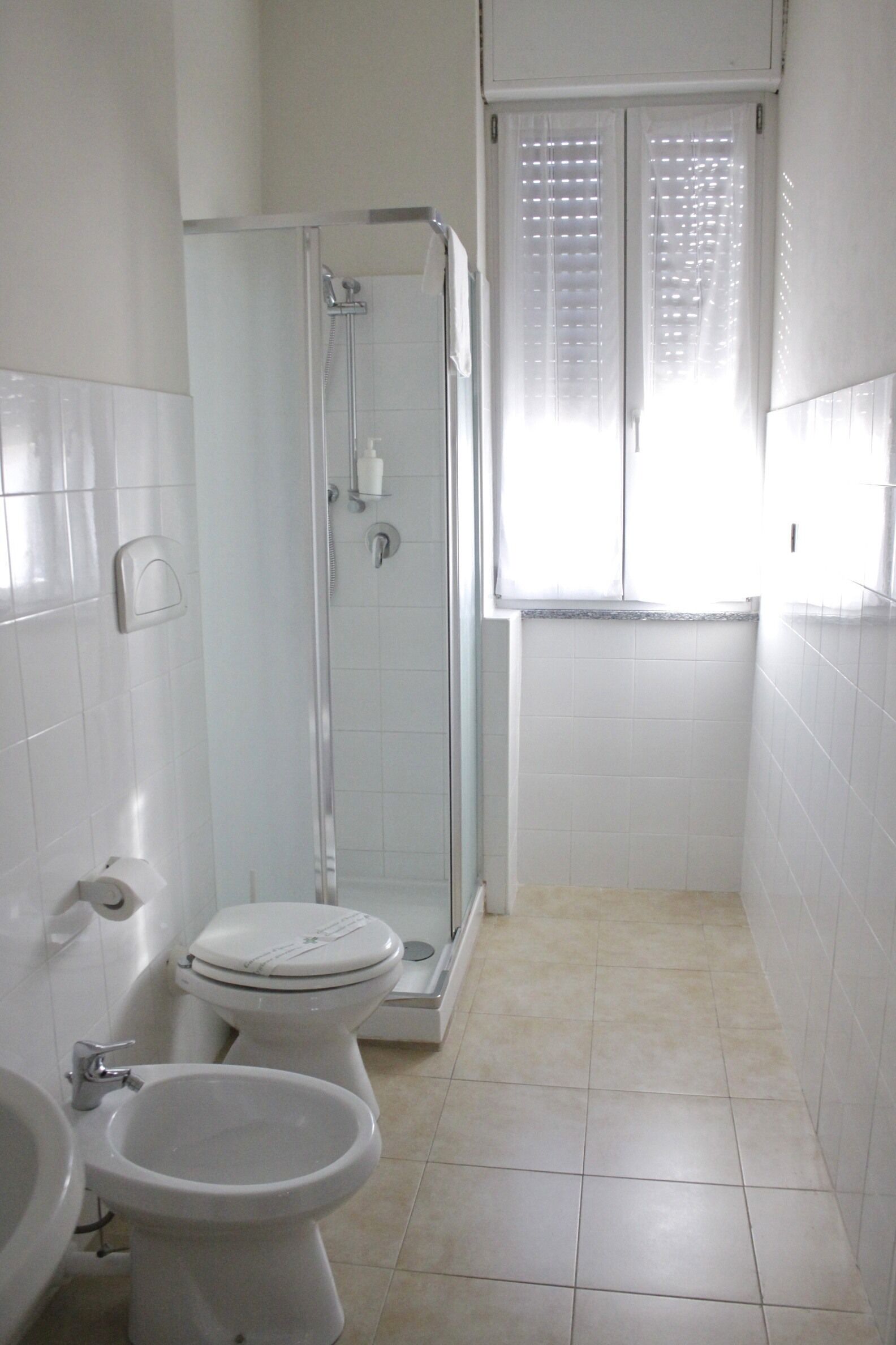 A small, white bathroom with a toilet, bidet, and shower stall.