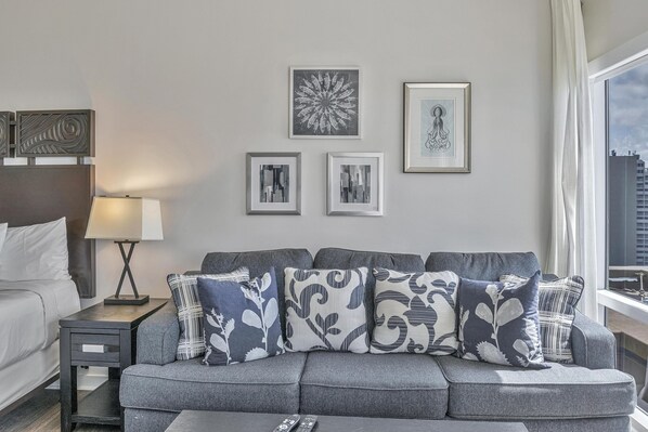 Un salon moderne avec un canapé gris, une petite table d’appoint avec une lampe et des œuvres d’art encadrées accrochées au mur.