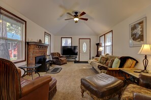 Una sala de estar acogedora con chimenea, muebles de cuero, ventilador de techo y televisor.