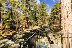 A river flowing through a forest with a metal railing and a chair by the railing. - Serene Creek Side Cottage Retreat (Banner)