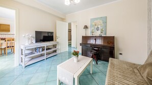 Un saló amb televisió, un piano, una taula amb un ram i un sofà.