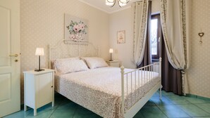Un dormitori amb llit, taulells de nit, un penjoll i cortines, i una obra d'art floral a la paret.