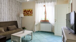 Un saló amb un sofà, una taula de centre, una televisió i una finestra amb cortines.