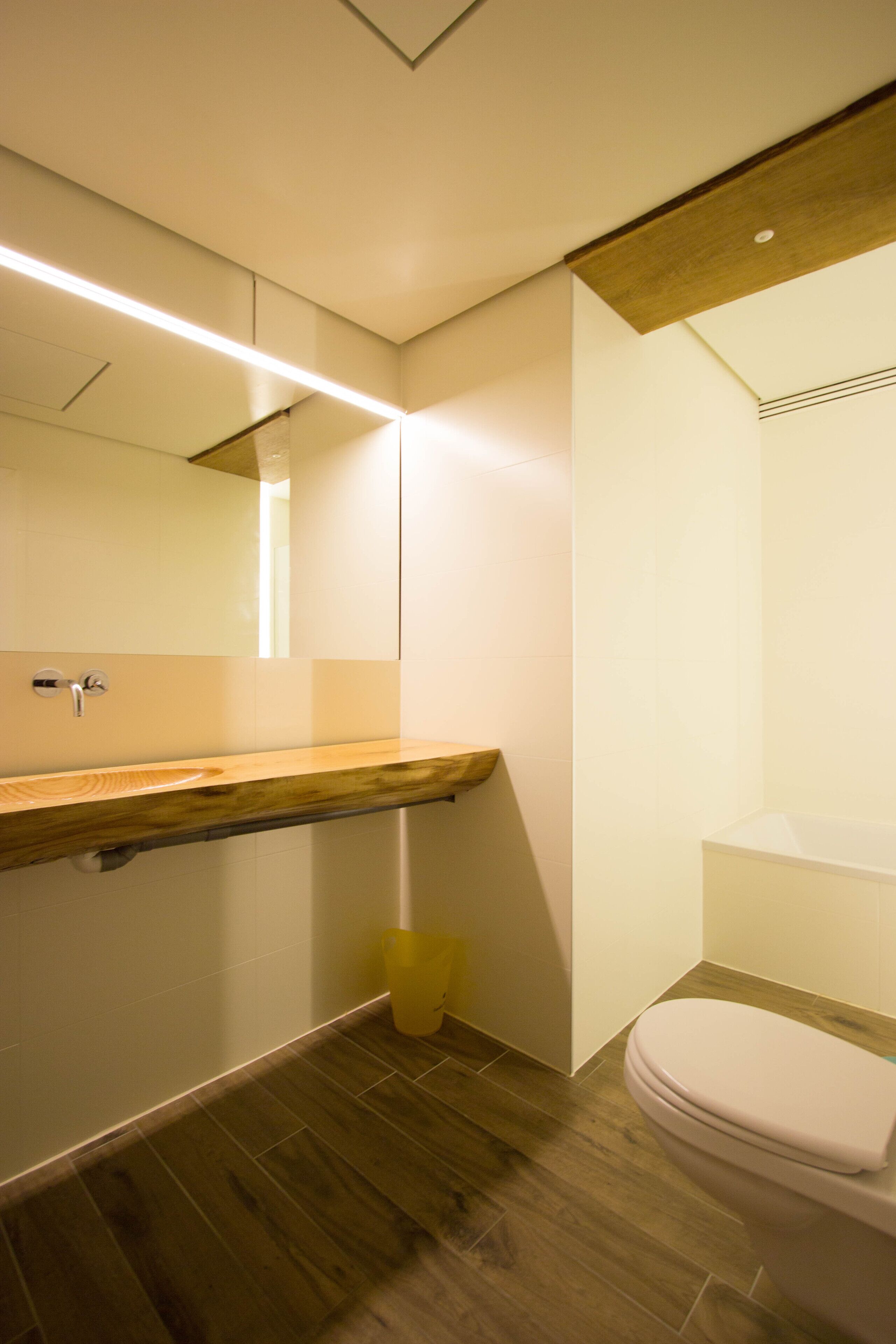 Een moderne badkamer met een houten wastafel, toilet en spiegel.