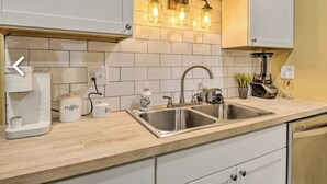 A kitchen with white cabinets, a double sink, a coffee machine, and a lighted backsplash. - Urban Chic Townhome Near Downtown (Indianapolis)