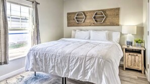 A bedroom with a bed, a ceiling fan, a window with curtains, and a wooden headboard with hexagonal decorations. - Urban Chic Townhome Near Downtown (Indianapolis)