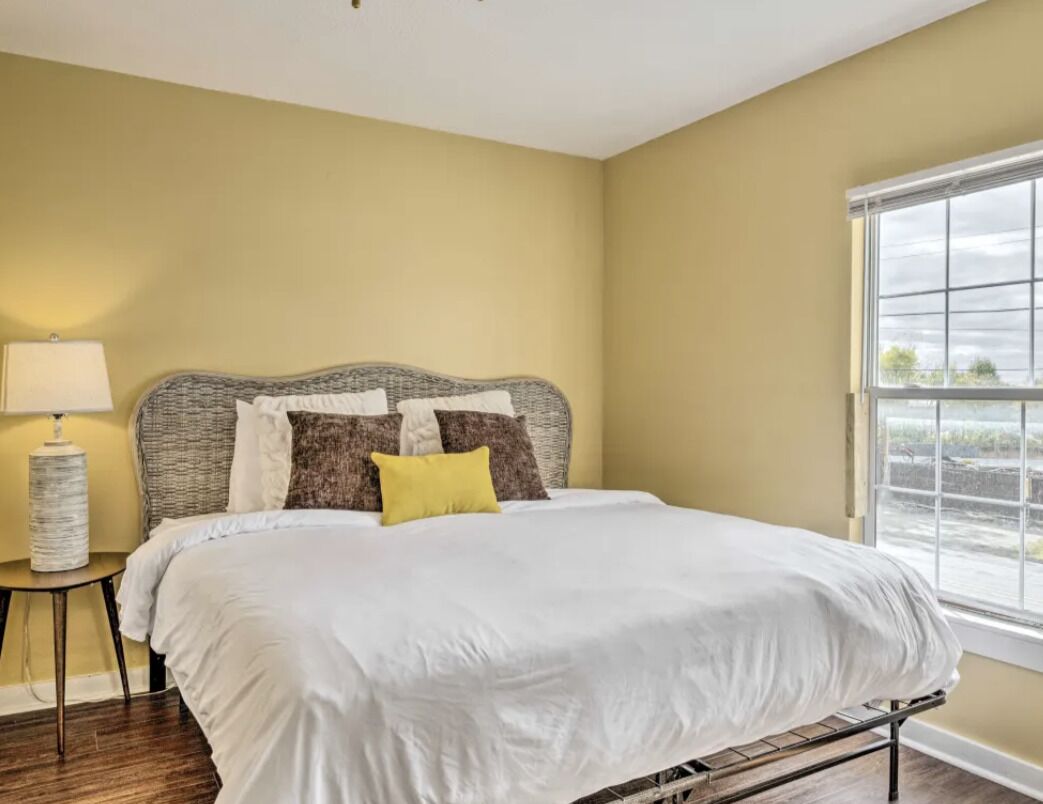 A bedroom with a bed, a nightstand, a lamp, and a window with a view.