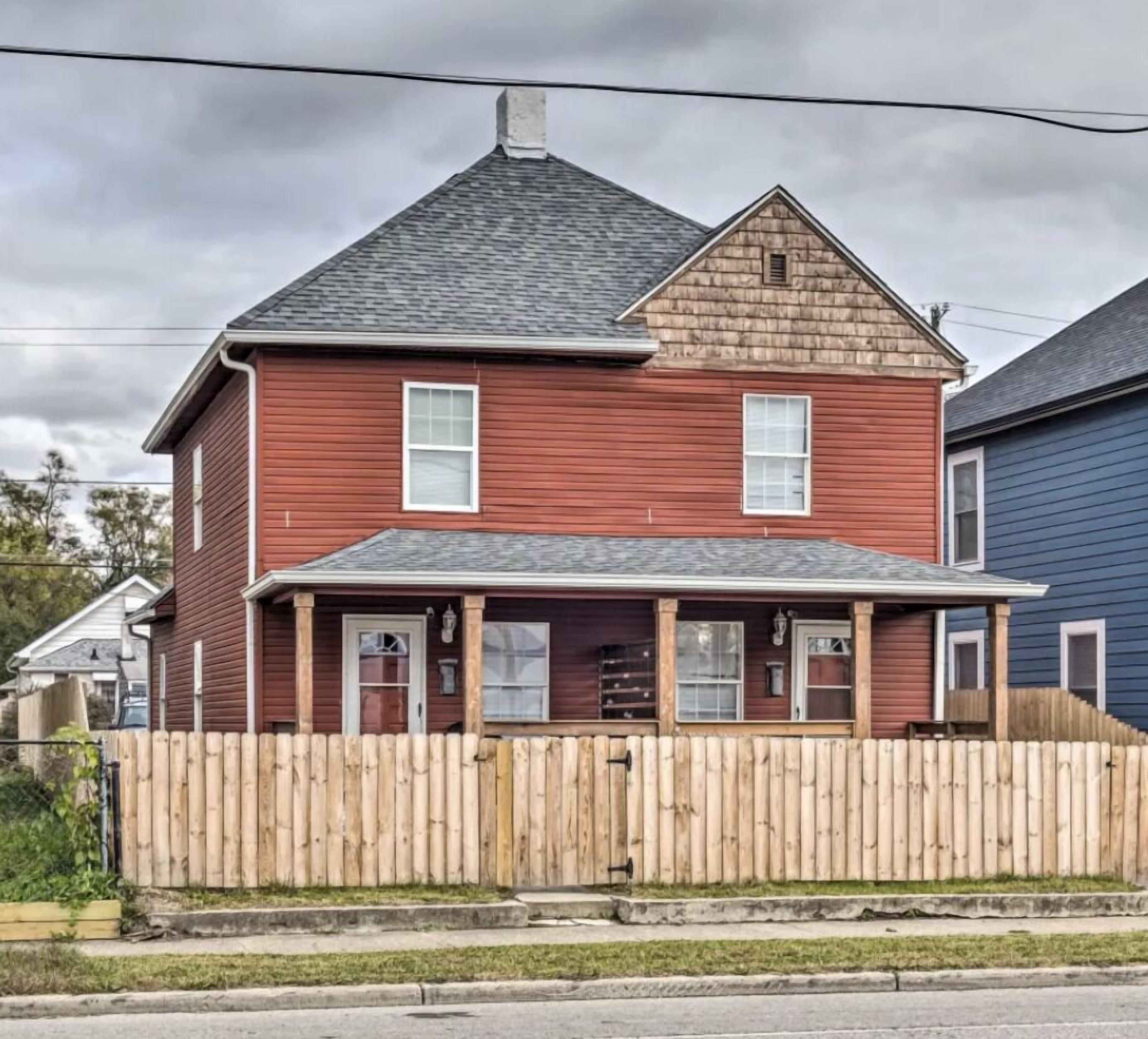 A two-story house with a red exterior, a grey roof, and a wooden fence in front.