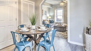 A dining area with a round table, blue chairs, and a plant. There is a living room in the background with a sofa and a ceiling fan. - Urban Chic Townhome Near Downtown (Indianapolis)