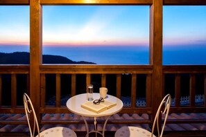 A wooden deck with a round table and two chairs, overlooking a scenic view of the sea and a distant landmass during sunset. - Vissala 4 Minuartia in Chortata (Lefkada)