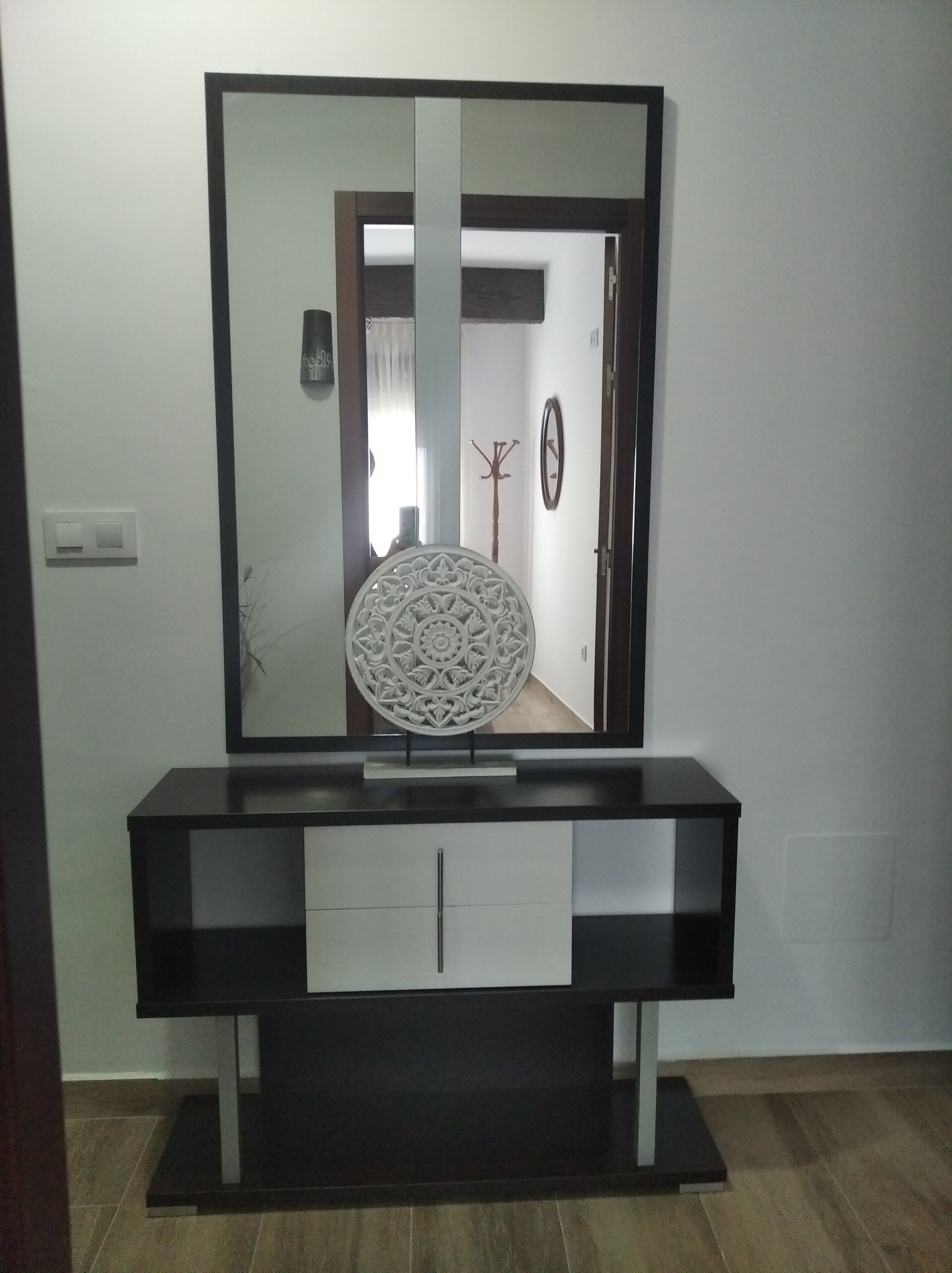 A modern vanity with a large mirror, a decorative wall piece, and a coat rack.