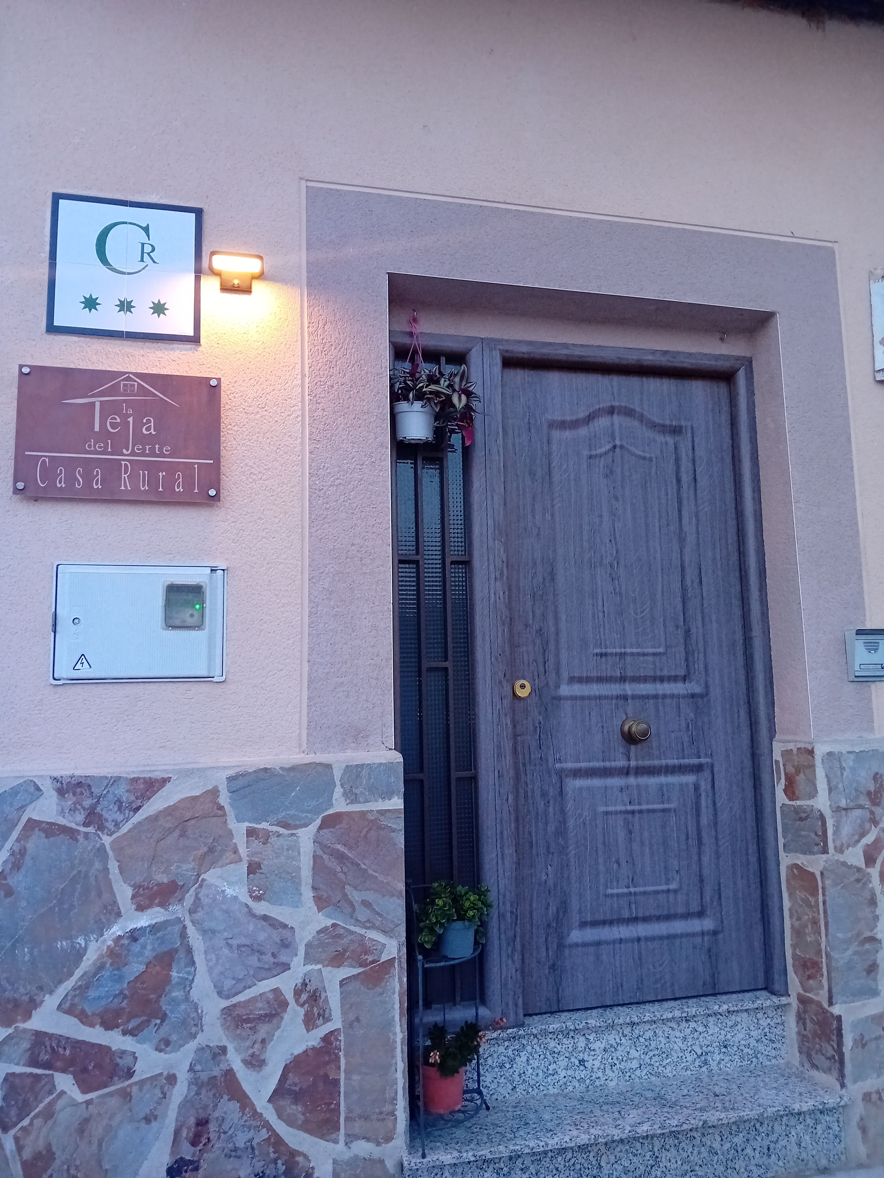 Une entrée rustique avec une porte en bois, une enseigne et un luminaire fixé au mur.