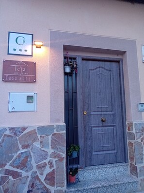 Une entrée rustique avec une porte en bois, une enseigne et un luminaire fixé au mur.