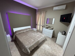 A bedroom with a bed, a bedside table, a dresser, a mirror, a TV, and an air conditioner. - Skycity b&b (Naples)