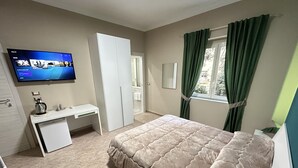 A bedroom with a bed, a desk, a television, and a window with curtains. - Skycity b&b (Naples)