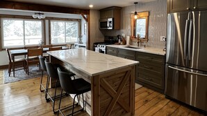 A modern kitchen with a central island, wooden flooring, and stainless steel appliances. - Valhalla!! (Ludlow)