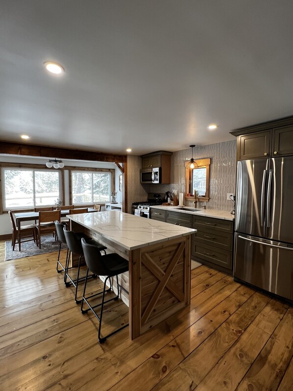 A modern kitchen with a central island, wooden flooring, and stainless steel appliances.