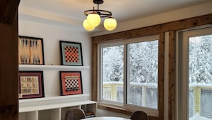 A cozy room with a round table and four chairs, a wooden ceiling, and a large window with a view of a snowy deck. - Valhalla!! (Ludlow)