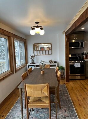 A dining area with a wooden table and chairs, a rug, and a kitchen with modern appliances.