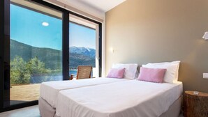 A bedroom with a large bed, a wooden side table, and a view of mountains through a glass door. - Villa Naya Desimi in Desimi (Lefkada)
