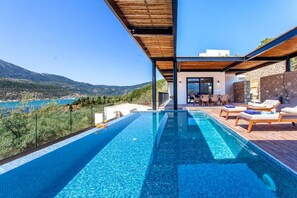 A modern infinity pool with a clear view of the sea and mountains, wooden deck, and lounge chairs. - Villa Naya Desimi in Desimi (Lefkada)