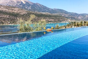 A swimming pool with clear blue water, surrounded by trees and mountains in the background. - Villa Naya Desimi in Desimi (Lefkada)