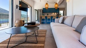 A modern living room with a sofa, a round table, and a kitchen in the background. - Villa Naya Desimi in Desimi (Lefkada)