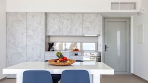 Una cocina moderna con encimera blanca, dos sillas azules y una cesta de fruta.