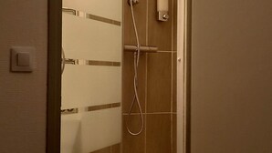 Een douche met een handdouche en een wandmengkraan, een zeepdispenser en een klein handdoekrek.