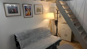 Een woonkamer met een bank, een bijzettafeltje, een lamp, een kapstok en een trap.