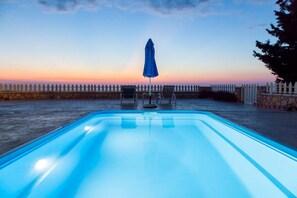Piscina com muro de pedra e cerca branca ao fundo.