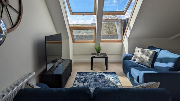 Une chambre de style loft moderne, dotée de fenêtres de toit, d’un grand miroir, d’une télévision et d’un canapé bleu.