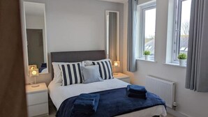 Une chambre à coucher avec un lit, des tables de chevet, un miroir et des fenêtres avec des rideaux.