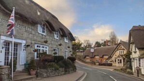A traditional stone building with a thatched roof, likely a pub or inn, with a flagpole and a signboard. - 2 Bed Apartment The Priory - Panoramic Sea View (Shanklin)