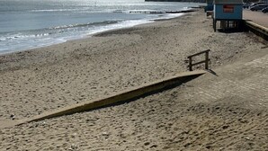A beach with a wooden walkway, a lifeguard station, and a rocky cliff in the background. - 2 Bed Apartment The Priory - Panoramic Sea View (Shanklin)