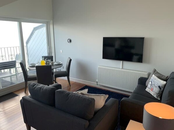 Una sala de estar moderna con televisor de pantalla plana, dos sofás, una mesa de centro y un comedor con sillas.