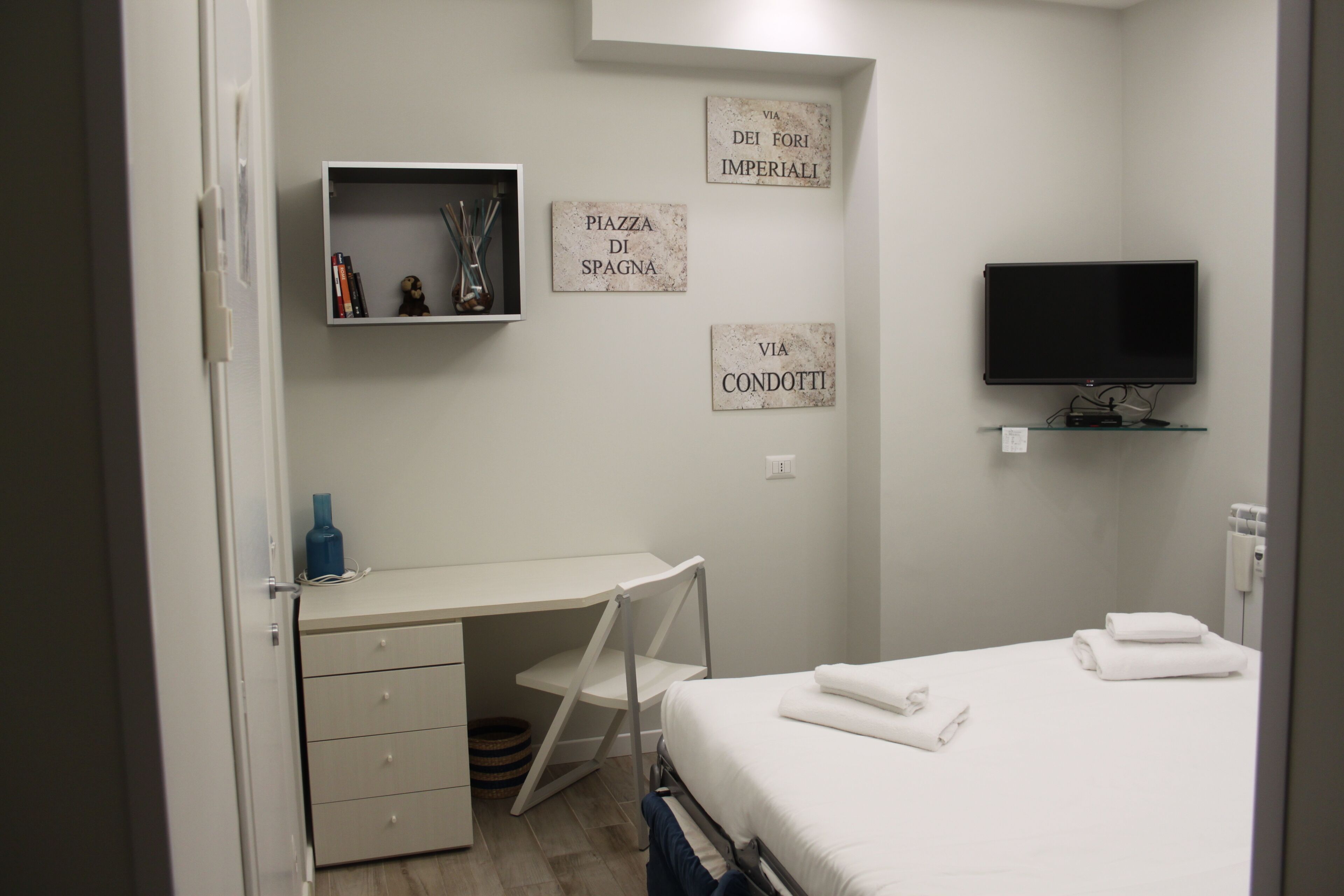 A bedroom with a bed, a desk, a television, and wall decorations.
