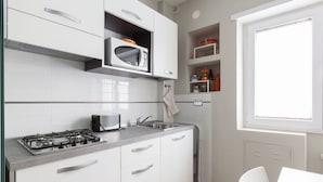 A modern kitchen with white cabinets, a gas stove, a microwave, and a window providing natural light. - A Passino from St. Peter's (Roma)