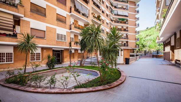 A multi-story residential building with balconies, a central courtyard with plants, and a paved walkway. - A Passino from St. Peter's (Roma)