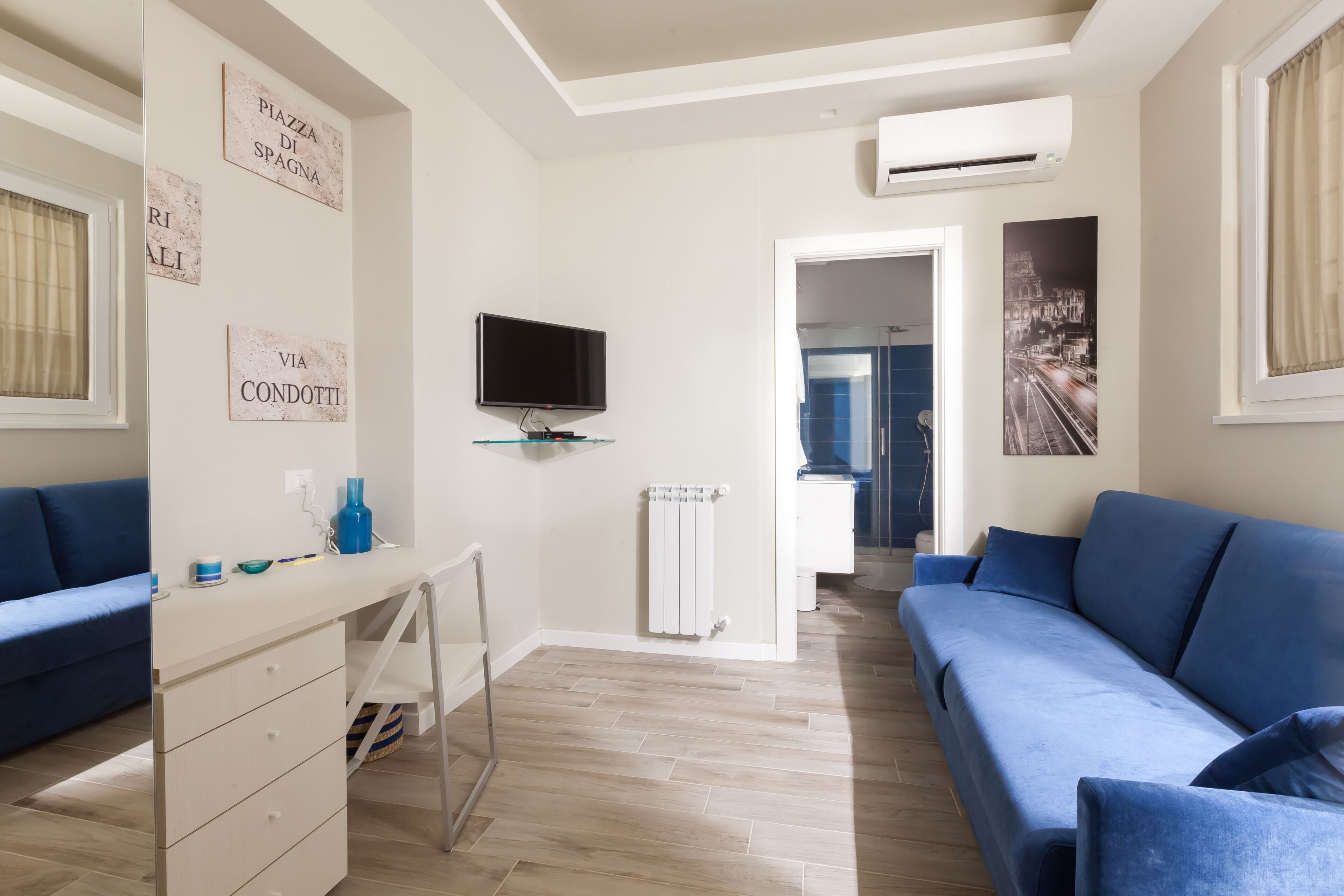 Ein modernes Wohnzimmer mit einem blauen Sofa, einem an der Wand montierten Fernseher und einer Heizung.