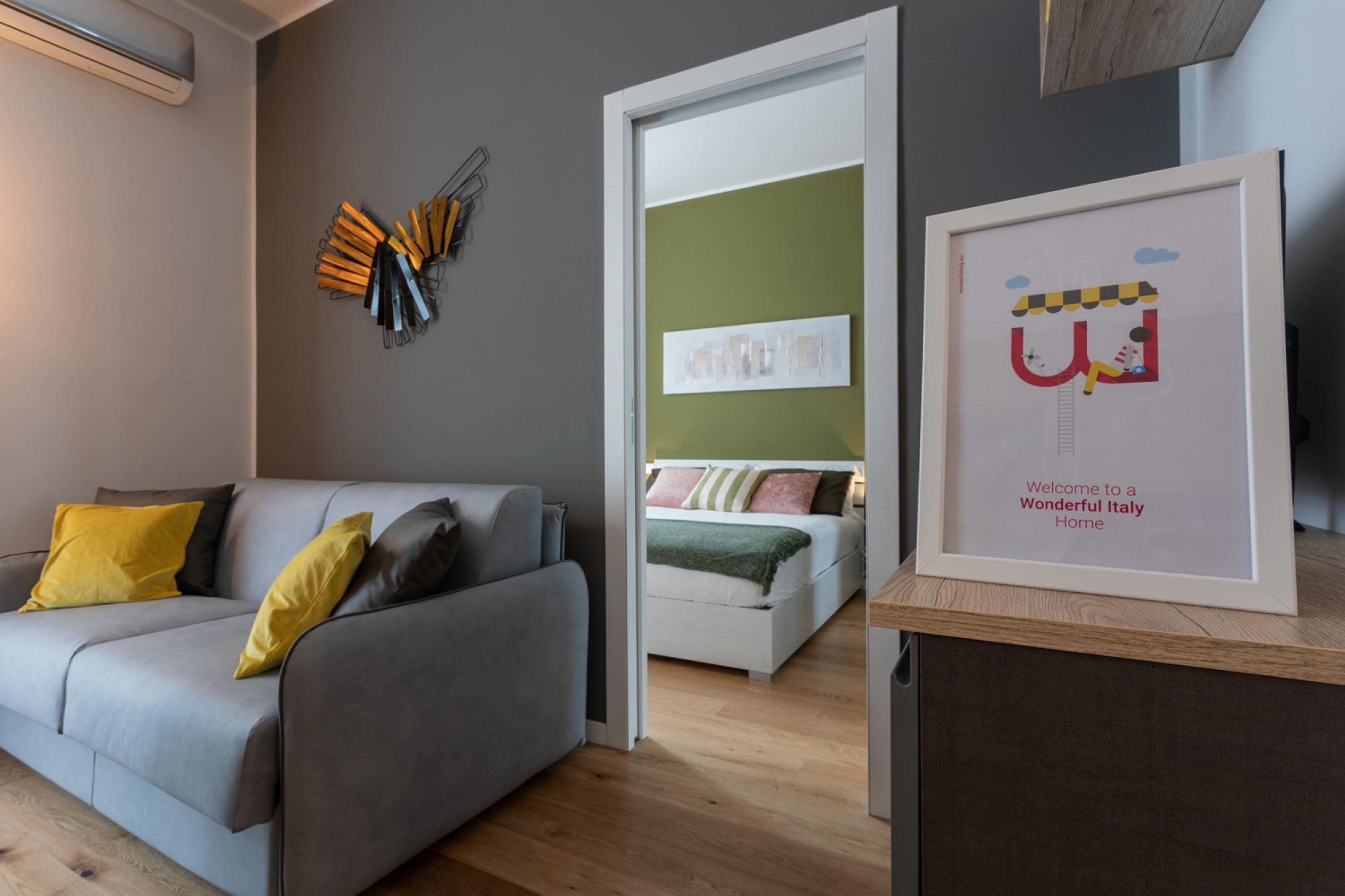 A modern living room with a grey sofa, a wooden coffee table, and a framed welcome sign.