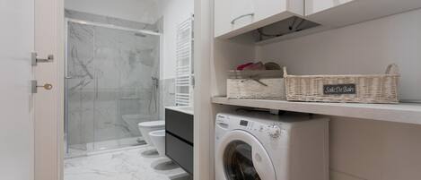 A modern bathroom with a glass shower enclosure, a washing machine, and a wicker basket labeled "Salle De Bain".