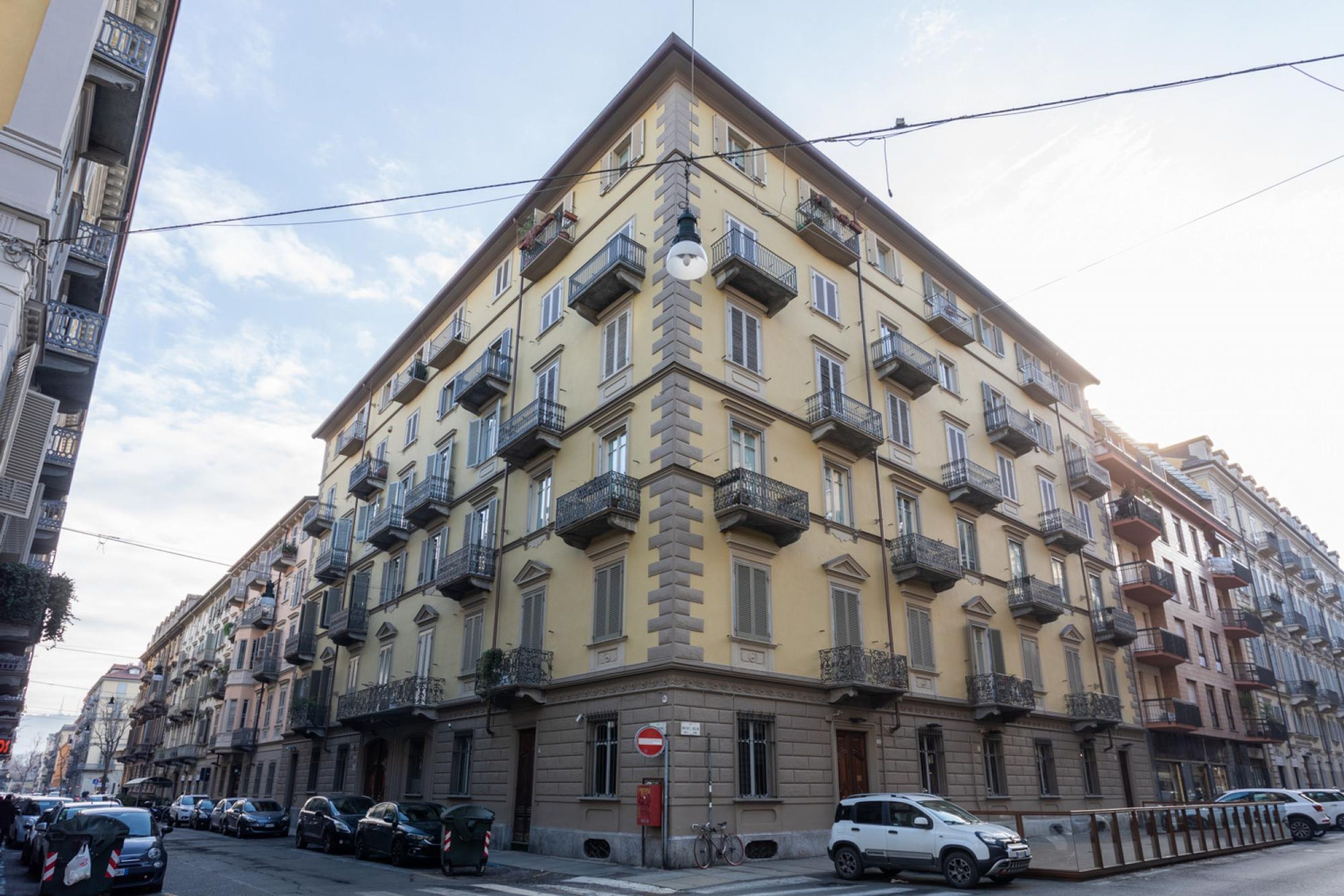 A multi-story building with balconies, a no entry sign, and parked cars on the street.