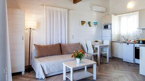 A cozy living room with a sofa, a coffee table with flowers, a dining table, and a kitchen area with a microwave and sink. - Vissala 5 Alkanna in Chortata (Lefkada)