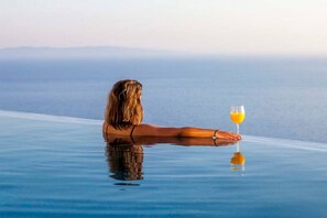 A person relaxing on an infinity pool with a glass of orange juice, overlooking a body of water. - Syvota 5 Sunset 1B Valentina (Igoumenitsa)