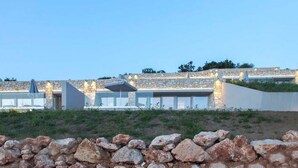 A modern building with stone walls and a flat roof, featuring large windows and outdoor seating areas. - Syvota 5 Sunset 1B Valentina (Igoumenitsa)
