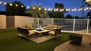 Eine Terrasse im Freien mit Feuerstelle, Sitzgelegenheiten und Lichterketten.